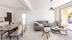 A modern living room with a dining area, a grey sofa, and a round coffee table. - Protaras Sol e Mar Villa 2 (Paralimni)