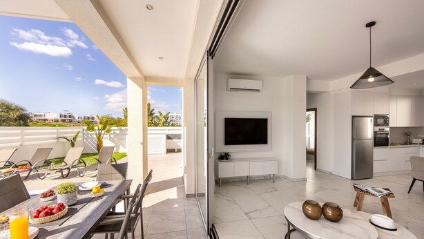 A modern living space with a dining area, kitchen, and a large TV. - Protaras Sol e Mar Villa 2 (Paralimni)