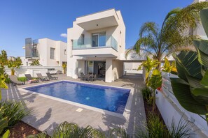 Une maison moderne à deux étages dotée d’une piscine, d’un espace salon extérieur et de plantes tropicales.