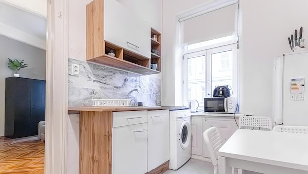 A modern kitchen with white cabinetry, a marble backsplash, and a built-in washing machine. - Beautiful 1BR Near Danube Praterstern (Vienna)
