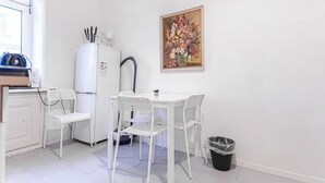 A small kitchenette with a white refrigerator, a sink, and a window. There is a white table with two chairs and a painting on the wall. - Beautiful 1BR Near Danube Praterstern (Vienna)