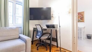 A room with a sofa, a desk with a computer, a TV, and a window with curtains. - Beautiful 1BR Near Danube Praterstern (Vienna)