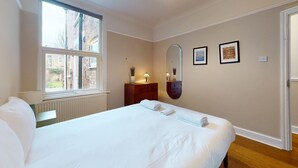 Una camera da letto ordinata con un letto grande, una cassettiera, uno specchio e una finestra con vista sugli edifici.