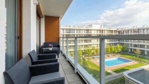 A balcony with wicker furniture, a view of a swimming pool, and a modern building complex in the background. - Seaside Apartment | 300 m to the Beach, Pool, Parking (Kołobrzeg)