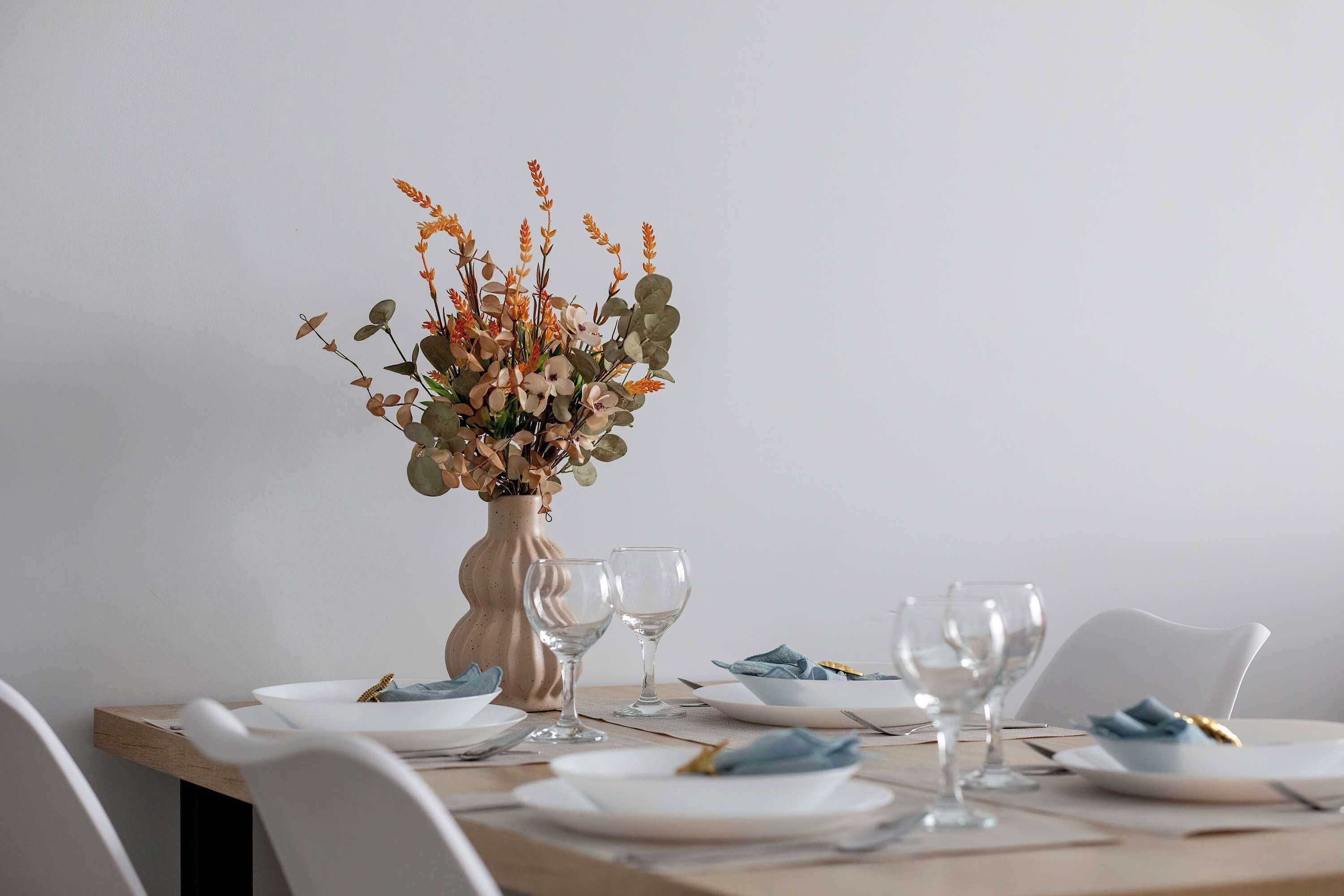 Una mesa de comedor dispuesta con platos, vasos y un jarrón de flores.