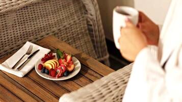 A wicker chair with a white plate of fruit and a cup of coffee on a wooden table.