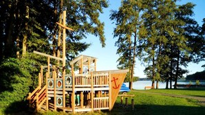 A wooden play structure with a flag, located near a lake. - Sunday Resort Hafendorf Junior Suite (Rheinsberg)