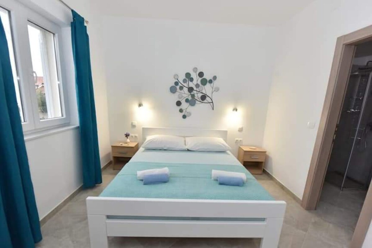 A bedroom with a bed, two bedside tables, a wall art piece, and a window with curtains.