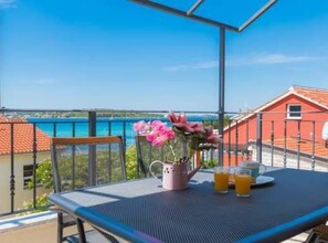 Un balcon avec une table, un vase de fleurs et deux verres de jus d’orange.