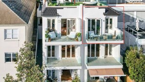 A modern multi-story residential building with a flat roof, large windows, and a balcony with outdoor furniture. - Sunny Side Up North Bondi (North Bondi)