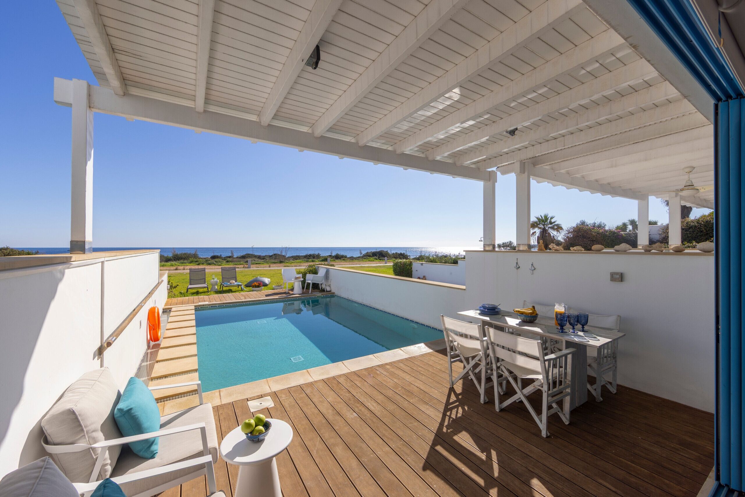 Un espace extérieur abrité avec une piscine, des meubles blancs et une vue sur l’océan.