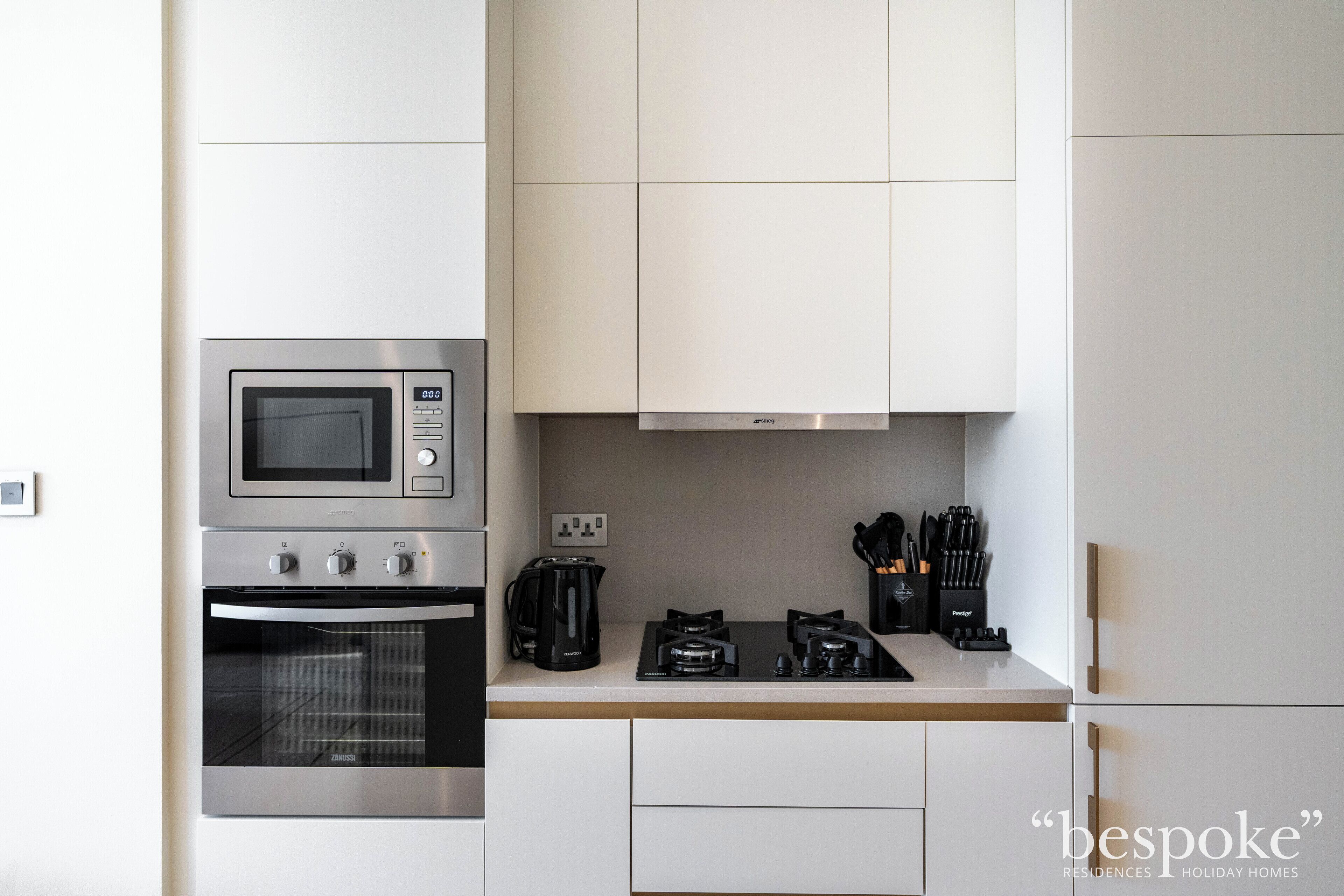 A modern kitchen with a built-in microwave, oven, and gas stove. There are white cabinets and a countertop with a coffee maker and utensils.