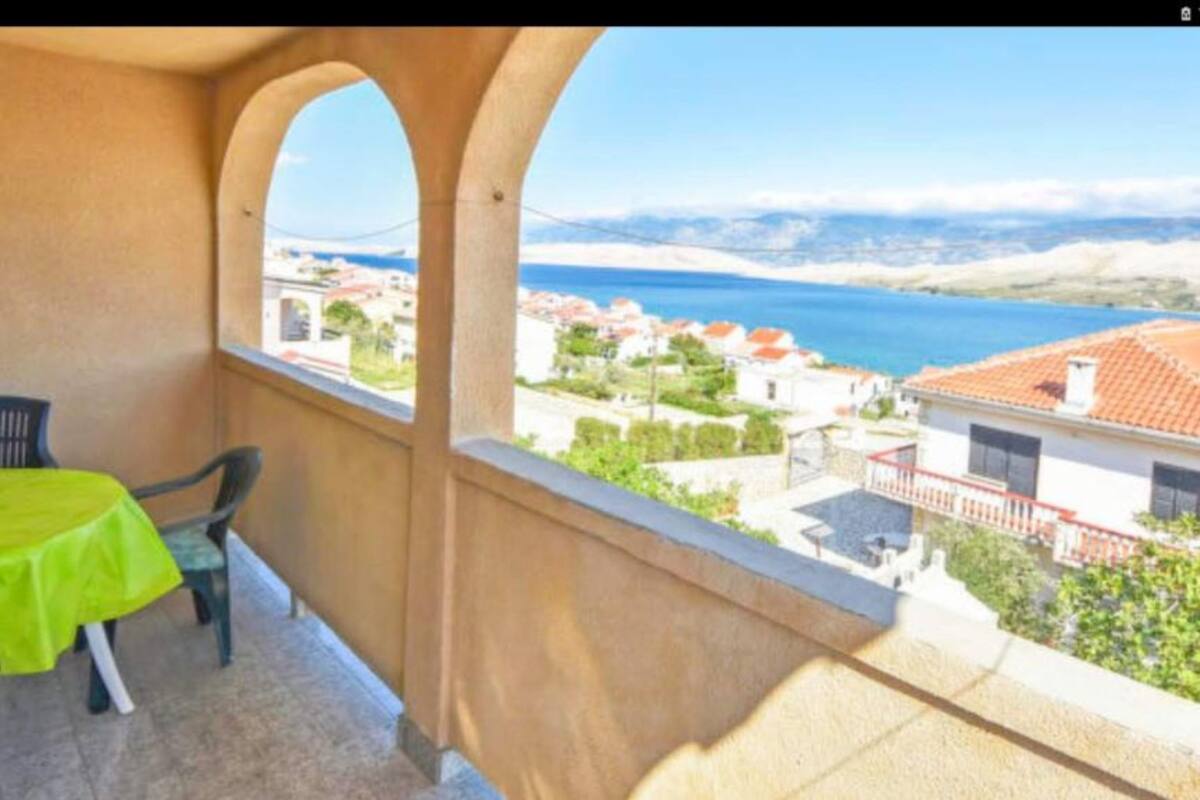 Un balcón con mesa y sillas, con vista a un pueblo costero con casas y una vista despejada del mar.