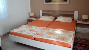 Un llit doble amb un edredó taronja i fulles estampades florals, dues taules de nit amb làmpades, un quadre d'un paisatge marítim a la paret i una finestra amb cortines.