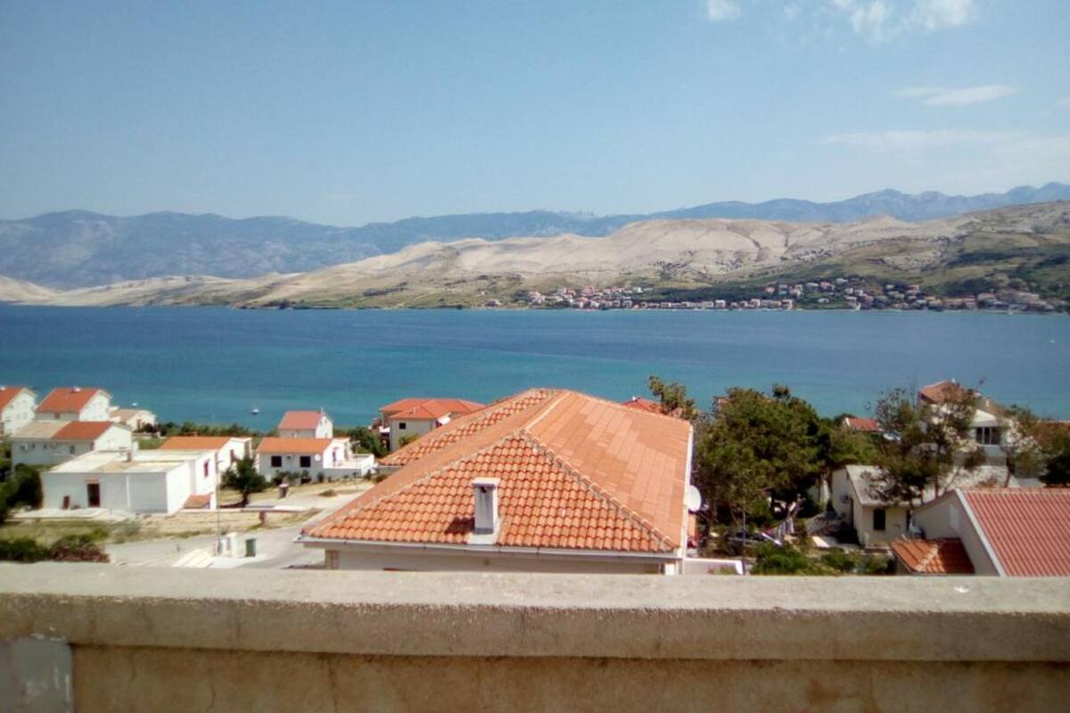 Un pueblo costero con casas de tejados color terracota, un mar azul transparente y montañas a la distancia.