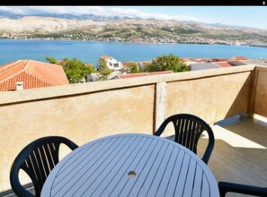 A terrace with a table and chairs, overlooking a body of water and a mountainous landscape. - Apartments Branka Pag (Pag)