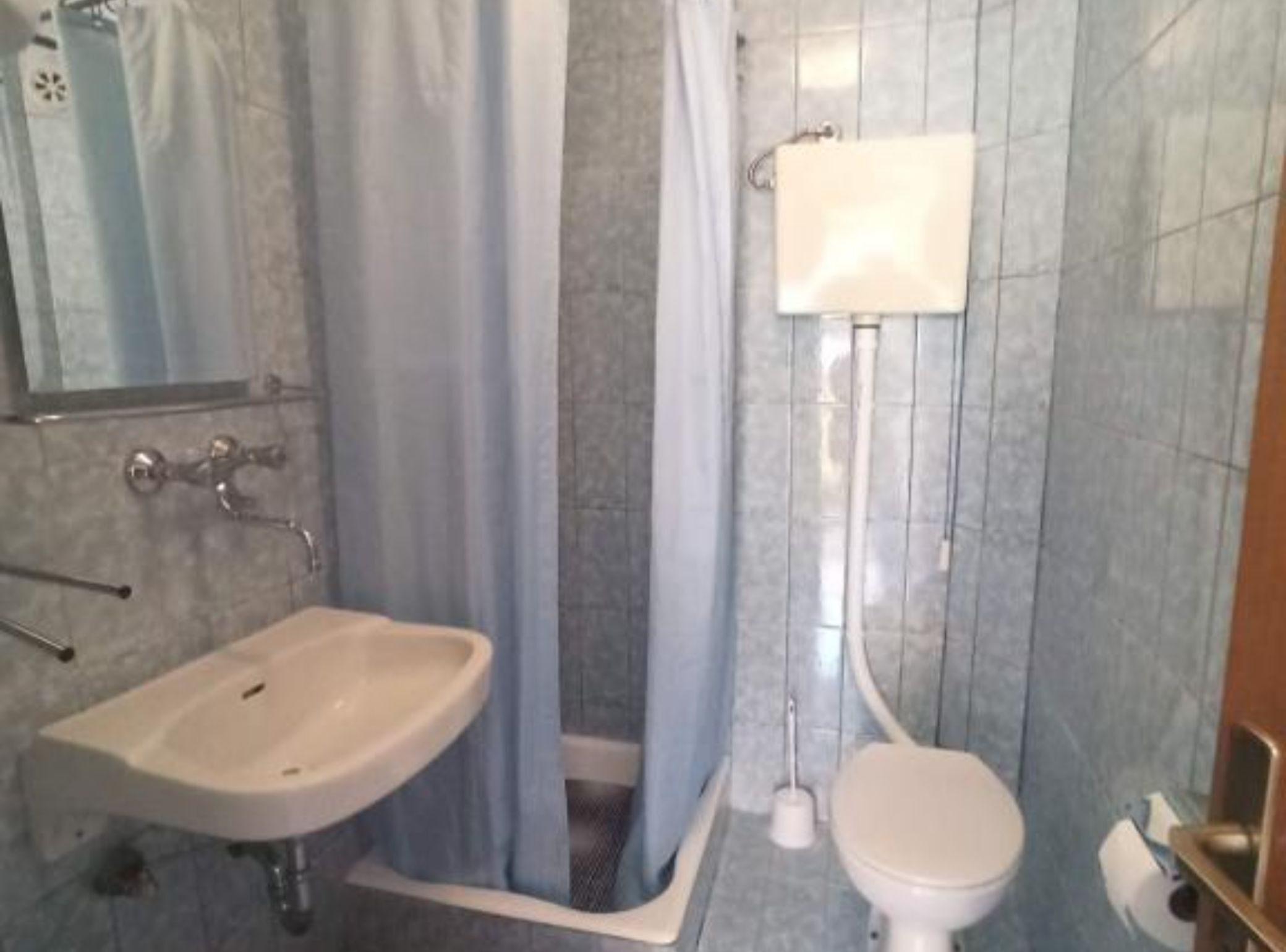 Un baño con lavamanos, inodoro, cortina de ducha y paredes de azulejos.