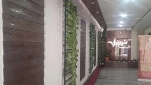 Un pasillo con alfombra roja, suelo de baldosas y una pared con persianas verticales y plantas verdes.