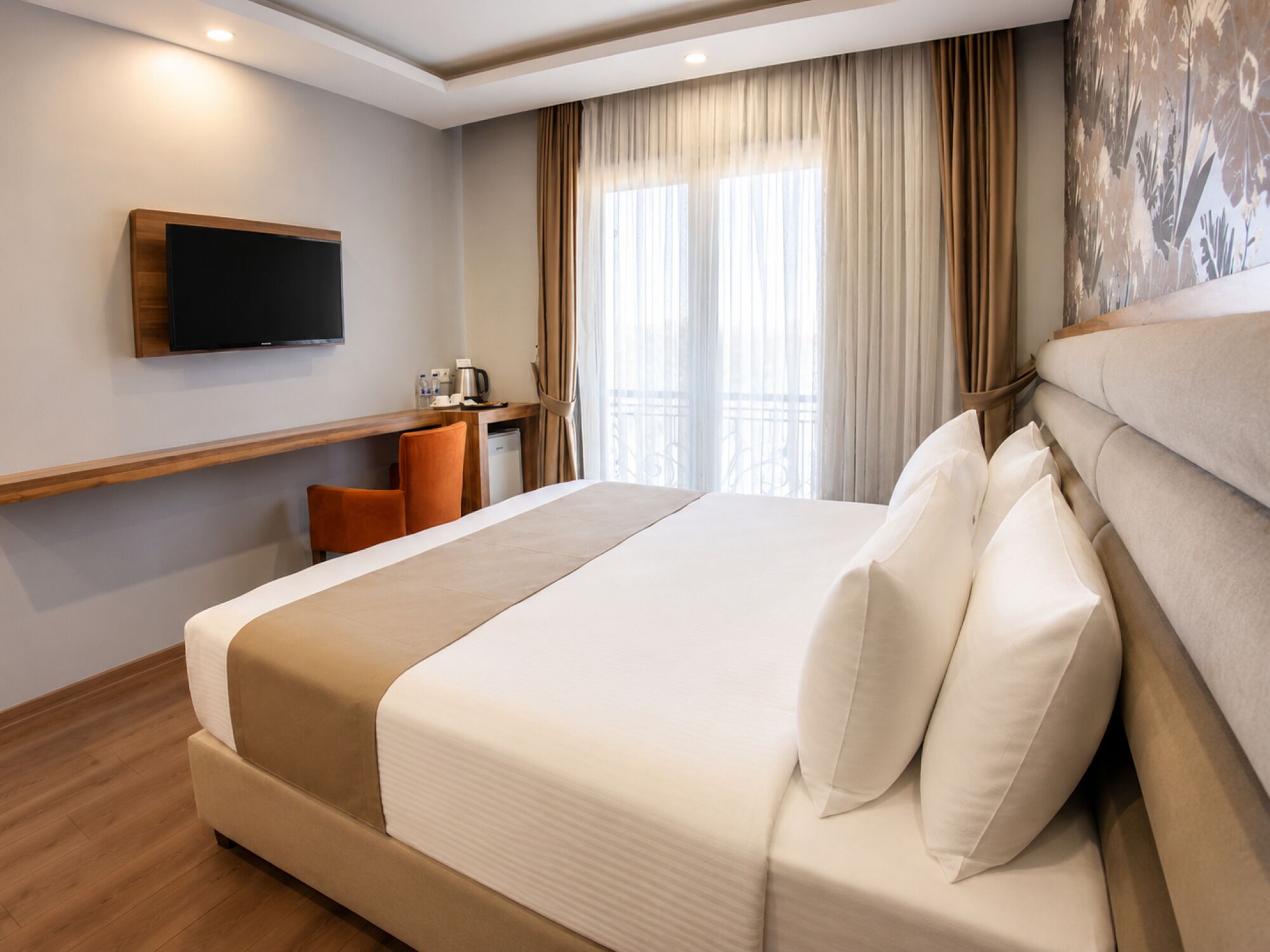 A hotel room with a bed, a TV, a desk, and a window with curtains.