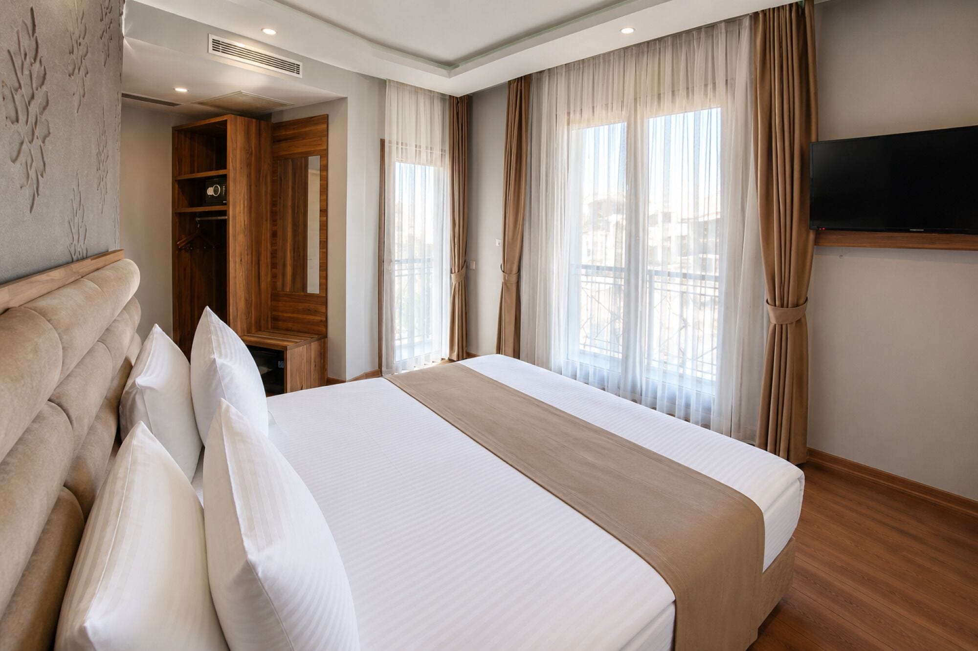 A hotel room with a large bed, a wardrobe, a television, and a window with curtains.