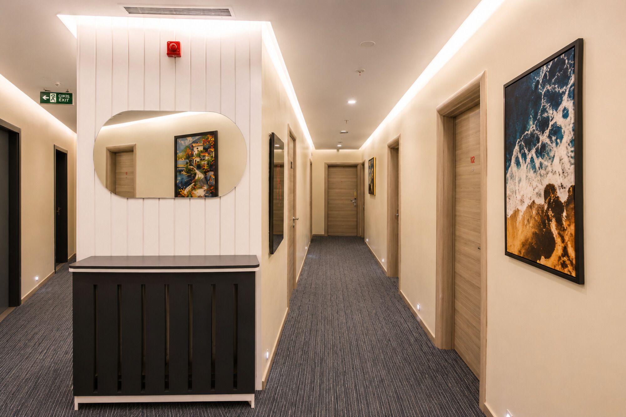 A hotel hallway with a reception desk, a fire alarm, and artwork on the walls.