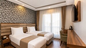 A hotel room with two beds, a wooden desk, a television, and a balcony with curtains. - Elite World Inn Istanbul Mahmutbey (Istanbul)