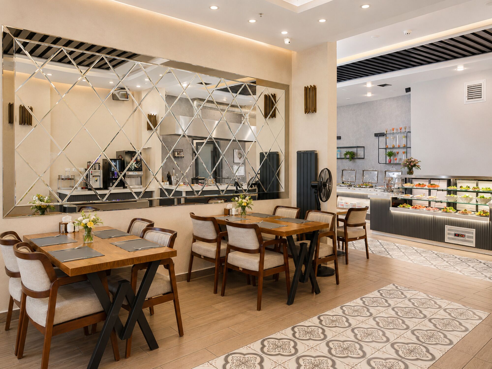 A modern dining area with wooden tables and chairs, a buffet with various food items, and a decorative wall with geometric patterns.