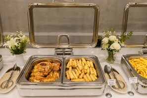 Ein reichhaltiges Buffet mit verschiedenen Speisen, darunter Chicken Wings, Frühlingsrollen und Pommes Frites.