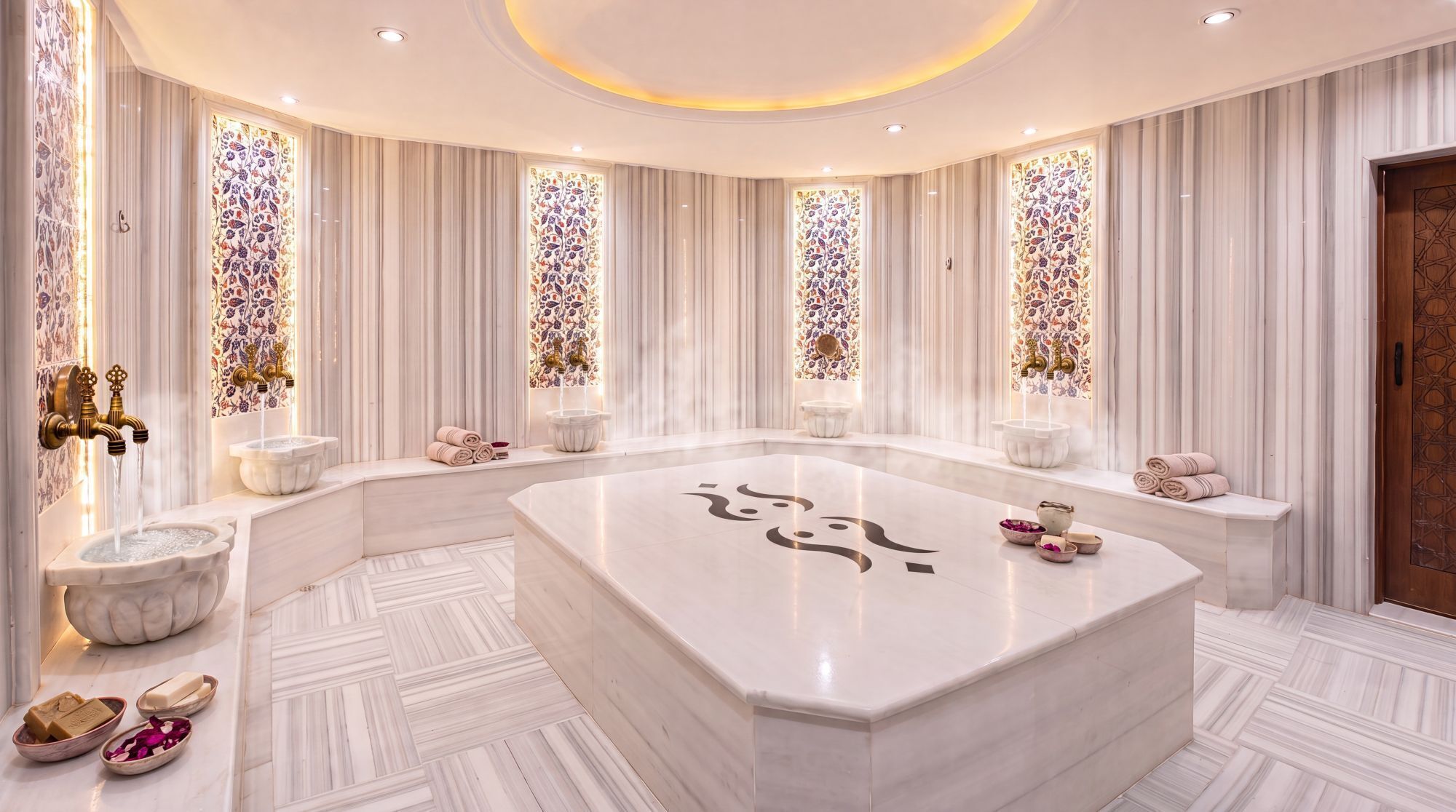 Un baño lujoso con lavamanos de mármol, una bañera grande y paneles decorativos en la pared.