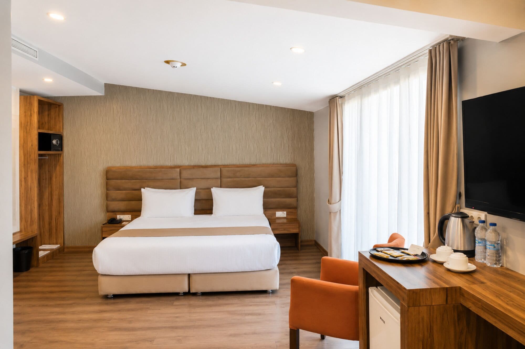 A hotel room with a bed, a desk with a chair, a television, and a minibar.