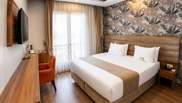 Habitación de hotel con cama, escritorio, silla, televisor y ventana con cortinas.