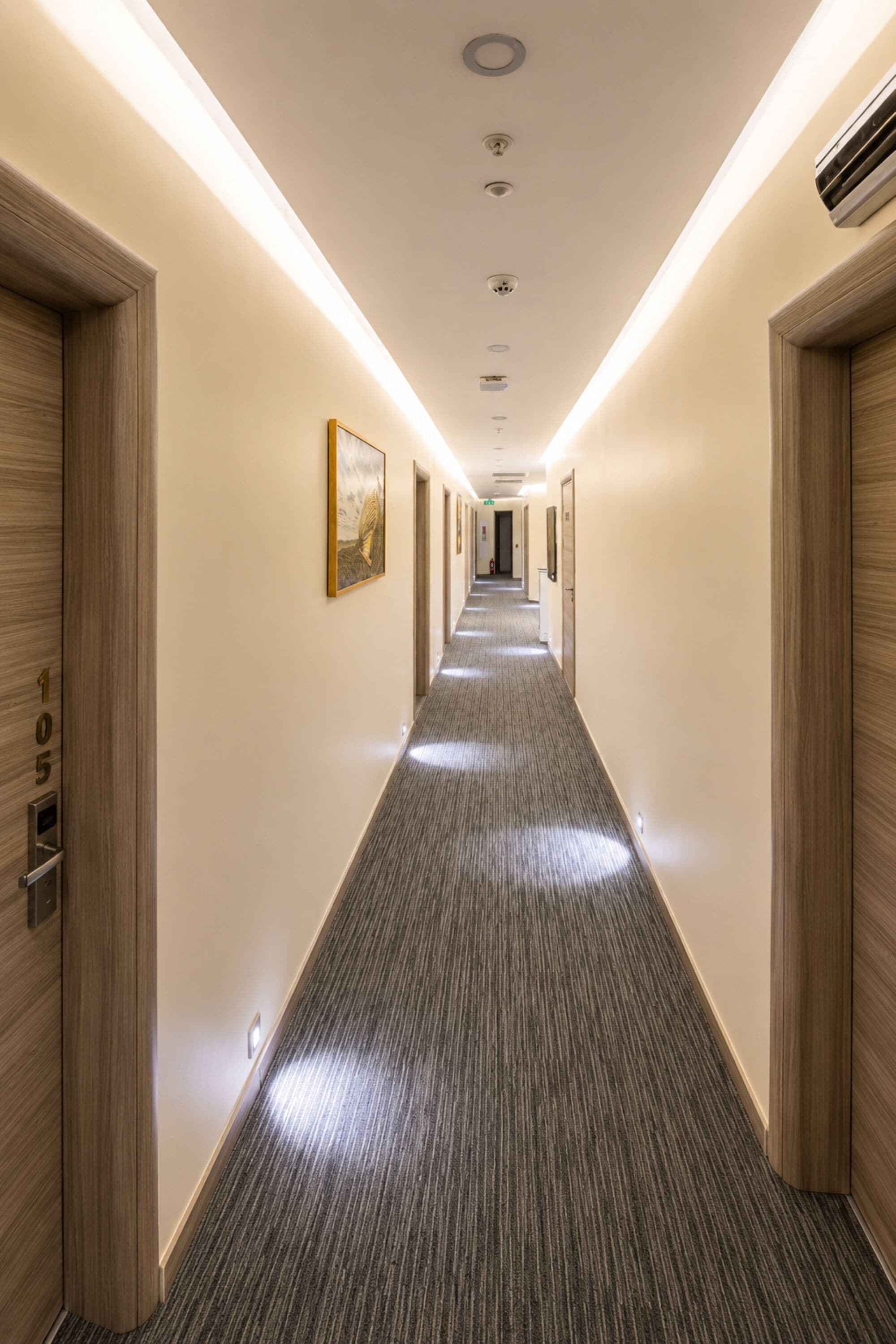 A hotel hallway with carpeted floors, wooden doors, and recessed lighting.