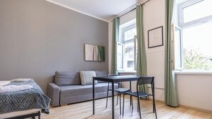 Une pièce comprenant un lit, un canapé gris, une table à manger avec des chaises, une fenêtre avec des rideaux et un tableau encadré accroché au mur.