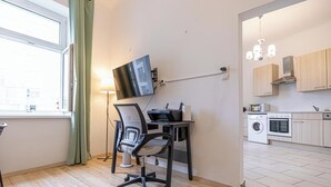 Un appartement moderne doté d’un plancher en bois, d’un bureau avec un ordinateur et une imprimante, d’un téléviseur fixé au mur et d’un coin cuisine comprenant un lave-linge et un four.