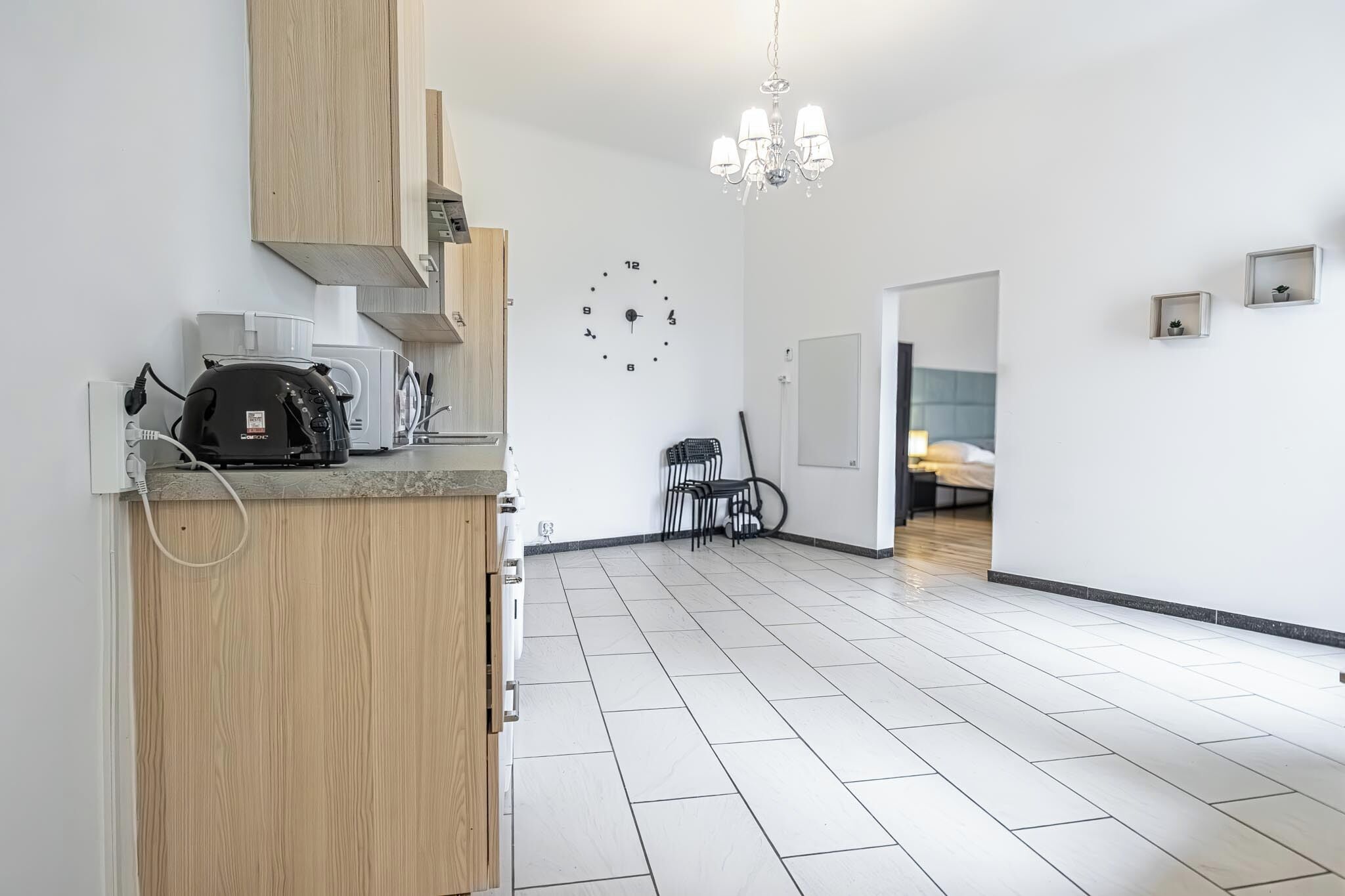 A modern kitchen with a coffee machine, a clock, and a chandelier.