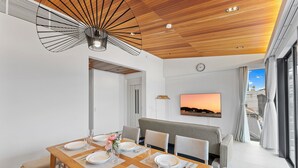 Ein modernes Esszimmer mit einem Holztisch, gedeckt für sechs Personen, einer Couch und einem an der Wand befestigten Fernseher.