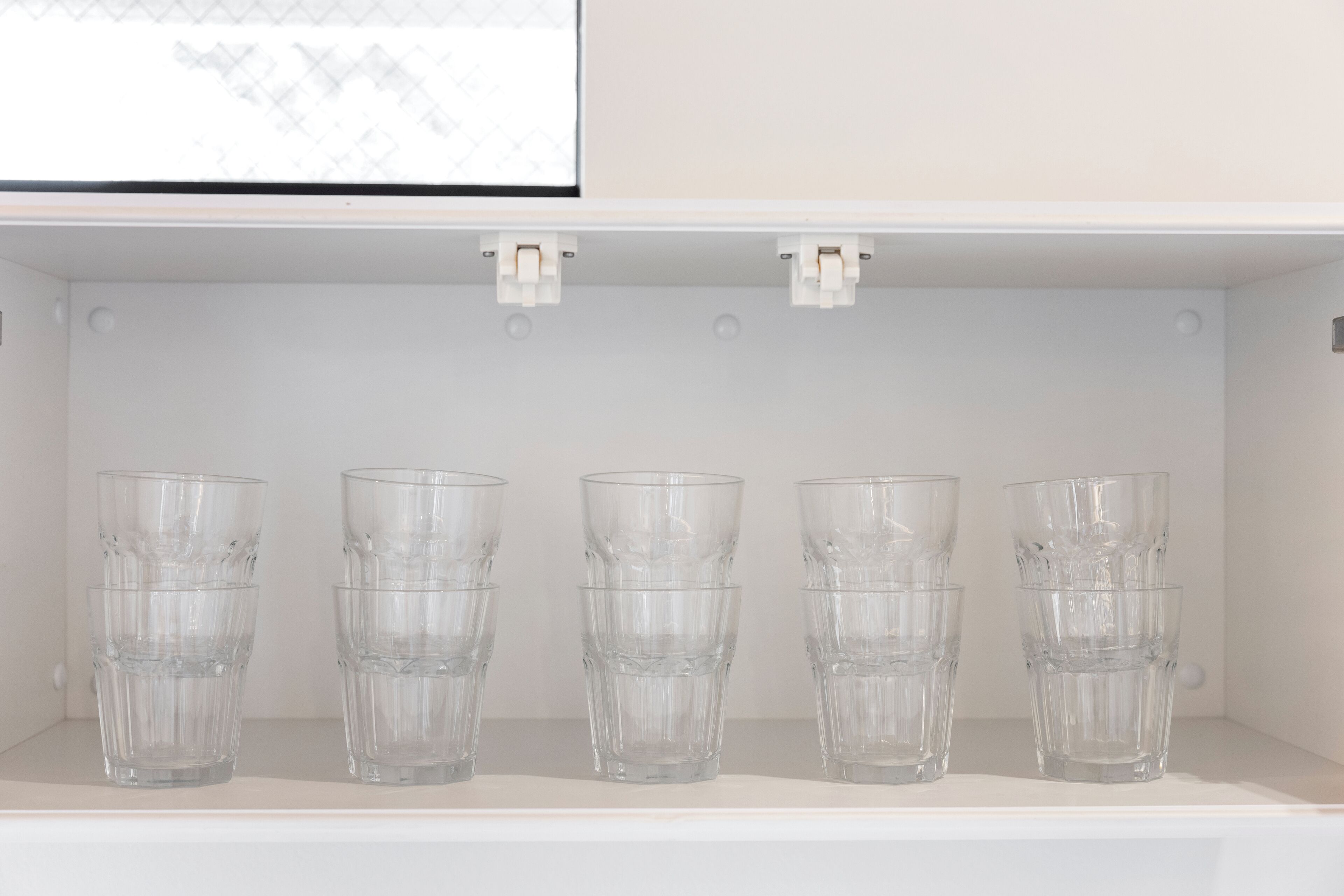 A white shelf with five clear glass tumblers.