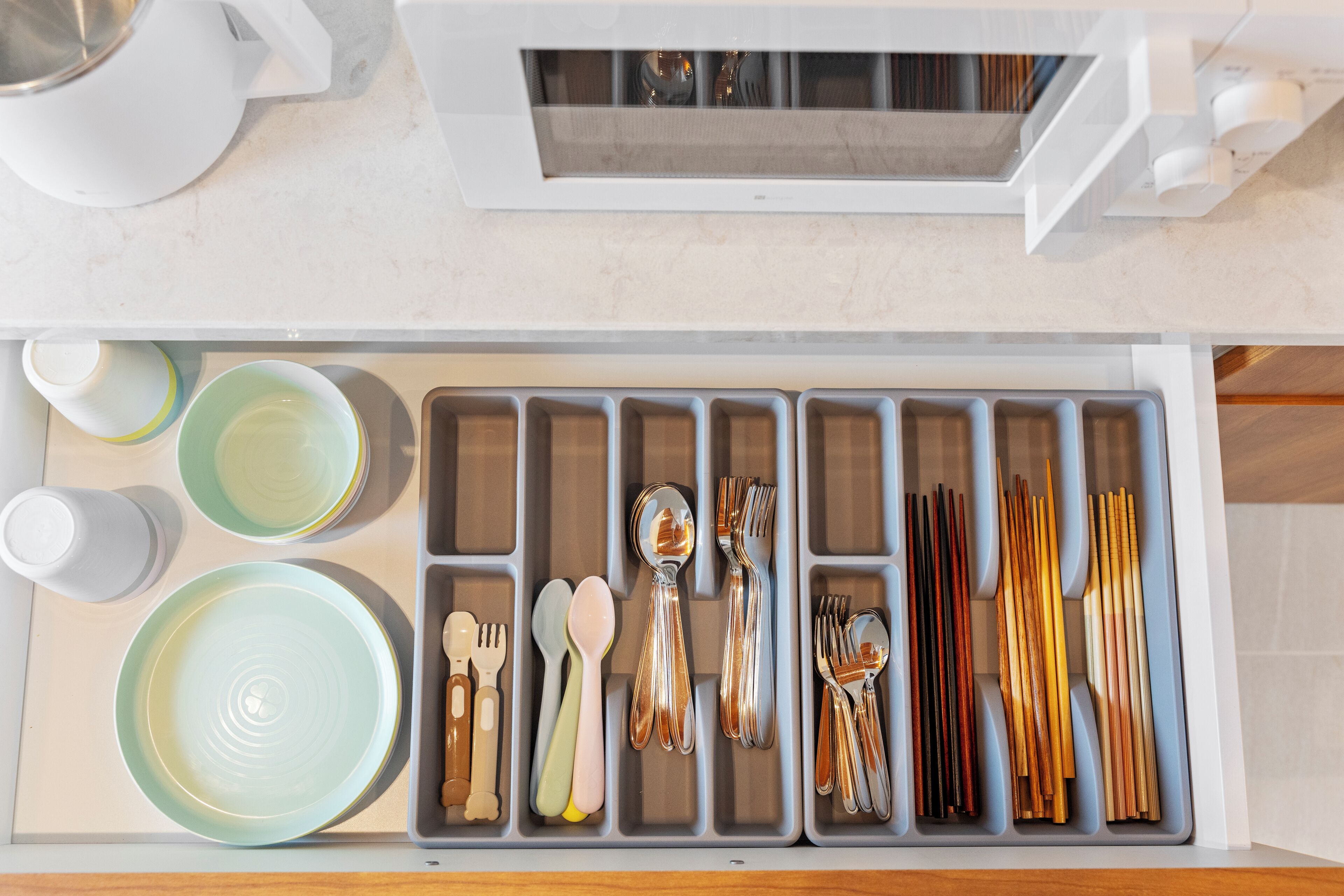 Un cajón de cocina con utensilios y vajilla organizados en compartimentos.