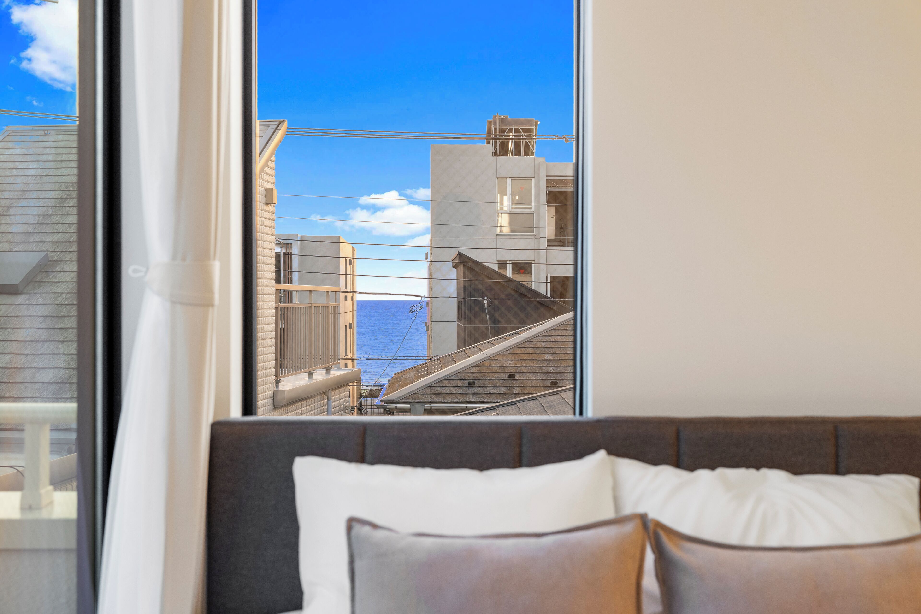 A bedroom with a large window overlooking a cityscape, a bed with a headboard, and a view of buildings and a body of water.