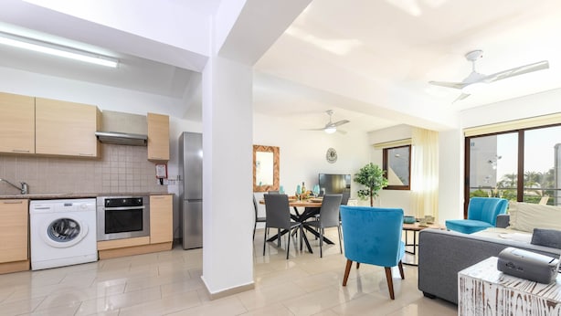 A modern kitchen with built-in appliances, a dining area with a table and chairs, and a living area with a sofa and a coffee table. - Nissi Apartment #101 (Ayia Napa)