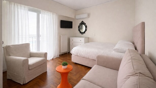 Un dormitorio con cama, dos sofás, una mesita con una planta, televisor y radiador.