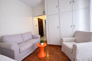 Ett vardagsrum med en grå soffa, en mönstrad fåtölj och ett litet orange bord med en växt.