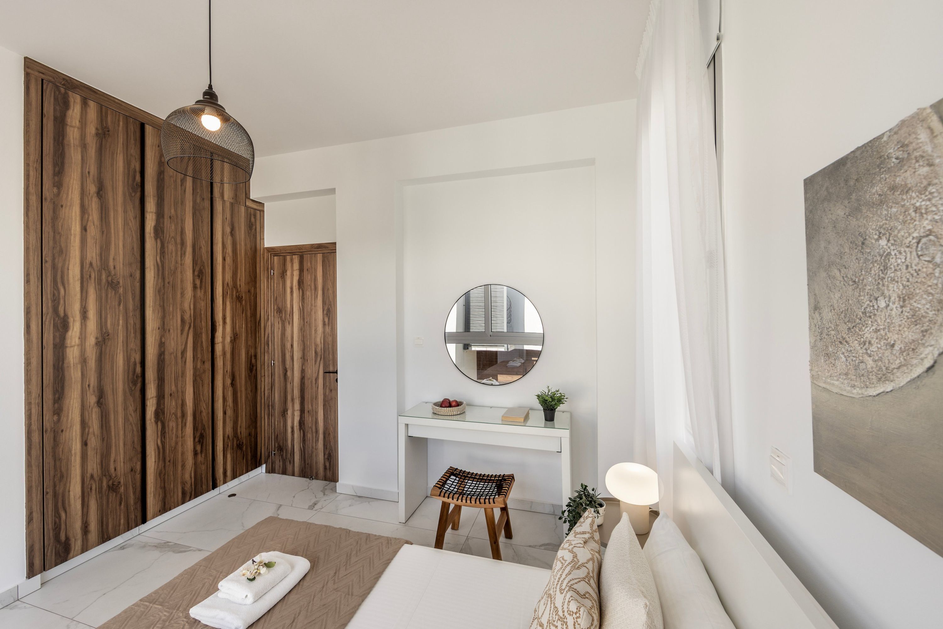 Een moderne kamer met een houten garderobe, een ronde spiegel boven een witte console en een groot abstract schilderij aan de muur.