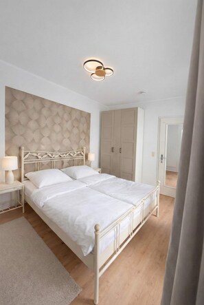 A bedroom with a large bed, wooden headboard, bedside lamps, and a wardrobe.