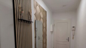 Ein Flur mit Holzboden, einem grauen Teppich, einem Wandspiegel, einer Zierleiste und einer Tür mit Lichtschalter.