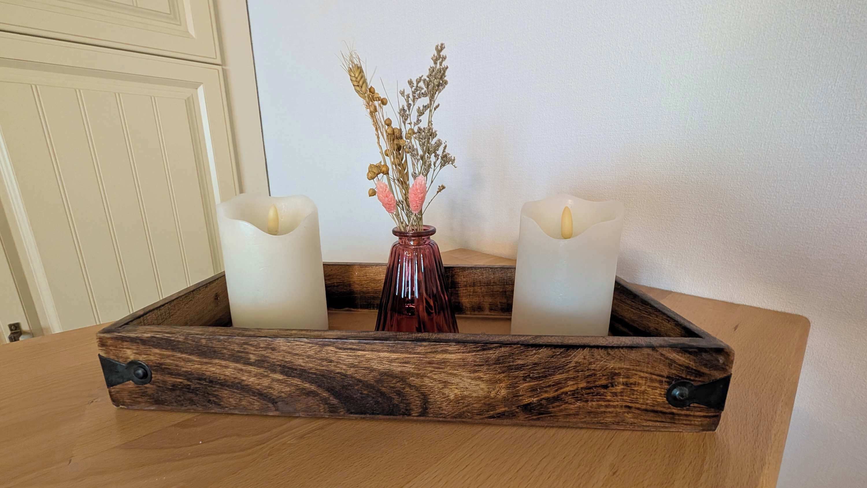 Ett träbricka med två ljus och en vas med torkade blommor.
