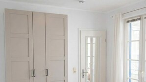 Ein Schlafzimmer mit großem Kleiderschrank, einem Bett mit weißer Bettwäsche und einer Deckenleuchte.