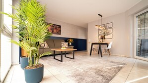 Ein modernes Wohnzimmer mit Sofa, Couchtisch und Essbereich. Kübelpflanzen und Kunstwerke sind an den Wänden angebracht.