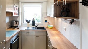 Eine moderne Küche mit Einbauofen, Mikrowelle und Spüle. Ein Holzregal mit Topfpflanzen und ein Topfhalter sind vorhanden.