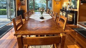 A spacious dining area with a large wooden table, surrounded by chairs, and a view of the outdoors through large windows. - Brecon Cottage | Serene 3BR Blue Mountains Escape (Leura)